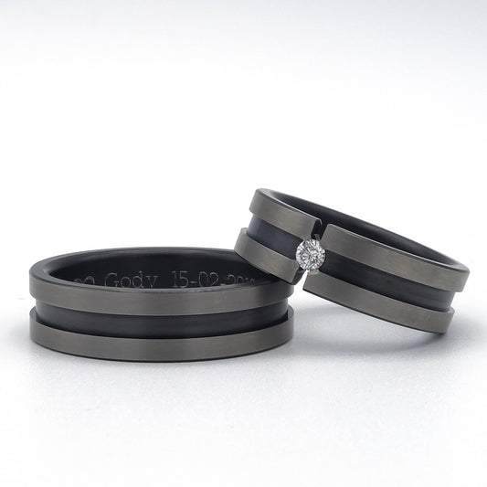 Twee zirkoniumringen met matte grijze randen; één ring met een briljant van 0.07ct in spanningszetting