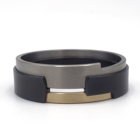 Aquila Black-ring van zirkonium, titanium en geelgoud – moderne ring met grafisch lijnenspel en sterk kleurcontrast.
