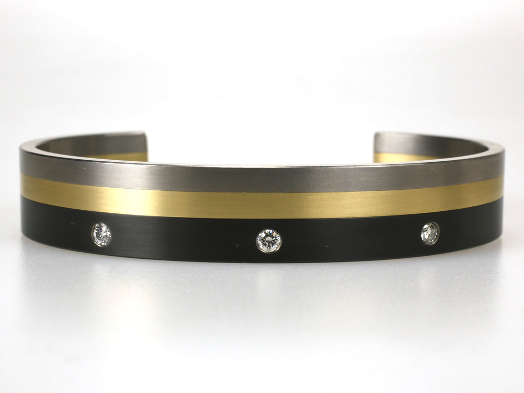 Titanium armband met zwart en geelgoud, voorzien van drie diamanten in zwarte titaniumlaag, strak en modern ontwerp.