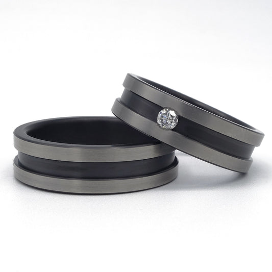 Twee zirkonium ringen met brede zwarte groef; één ring met diamant van 0.08 ct en één zonder, op een witte achtergrond.