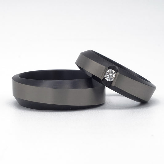 Set van twee zirkonium trouwringen met golvend profiel; één ring met een diamant in spanningszetting, één zonder steen.