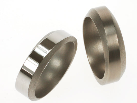 Twee titanium ringen met golvend profiel; één met glanzende buitenkant en matte facetten, één volledig mat.