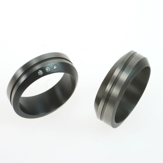 Set van twee zirkonium trouwringen met golvend profiel en zwarte lijn; één ring met drie diamanten, één zonder.