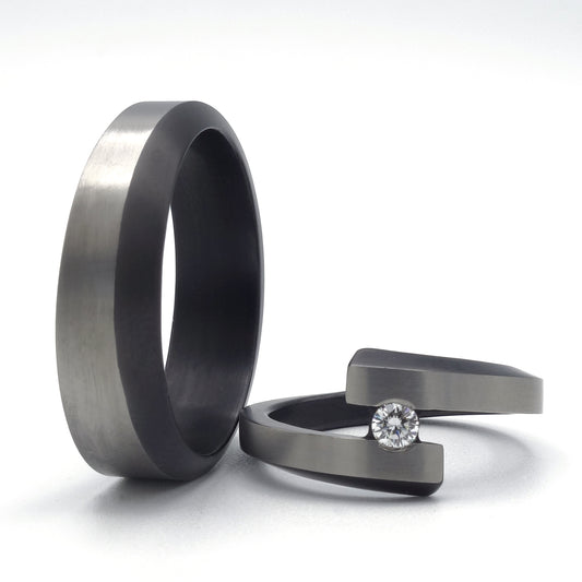 Set van twee zirkonium trouwringen: één ring met open spanningszetting en diamant, de andere glad en golvend gevormd.