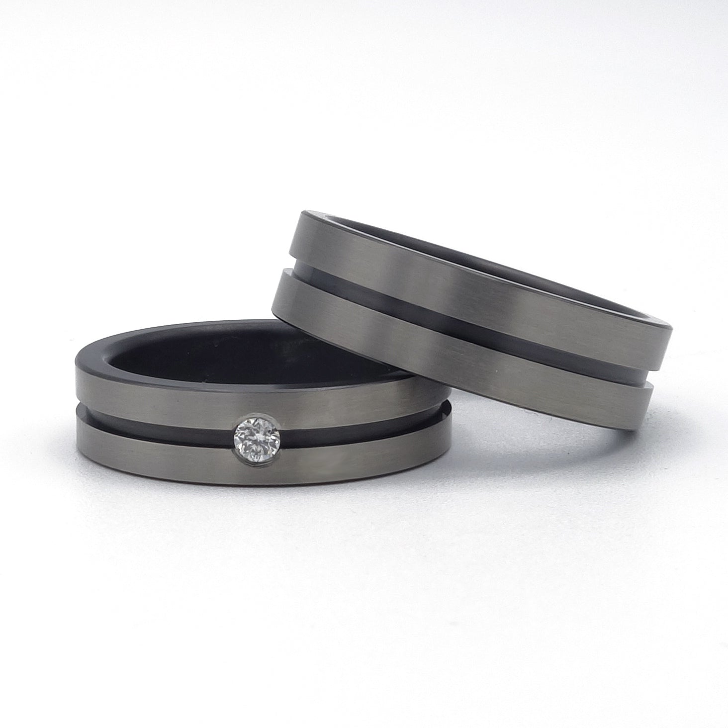 Twee zirkonium ringen met zwarte lijn; één ring met diamant en één zonder, gefotografeerd op een witte achtergrond.