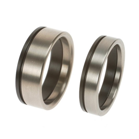 Trouwringenset van titanium met verzonken zirkoniumlijn, brede herenring en smallere bijpassende ring.