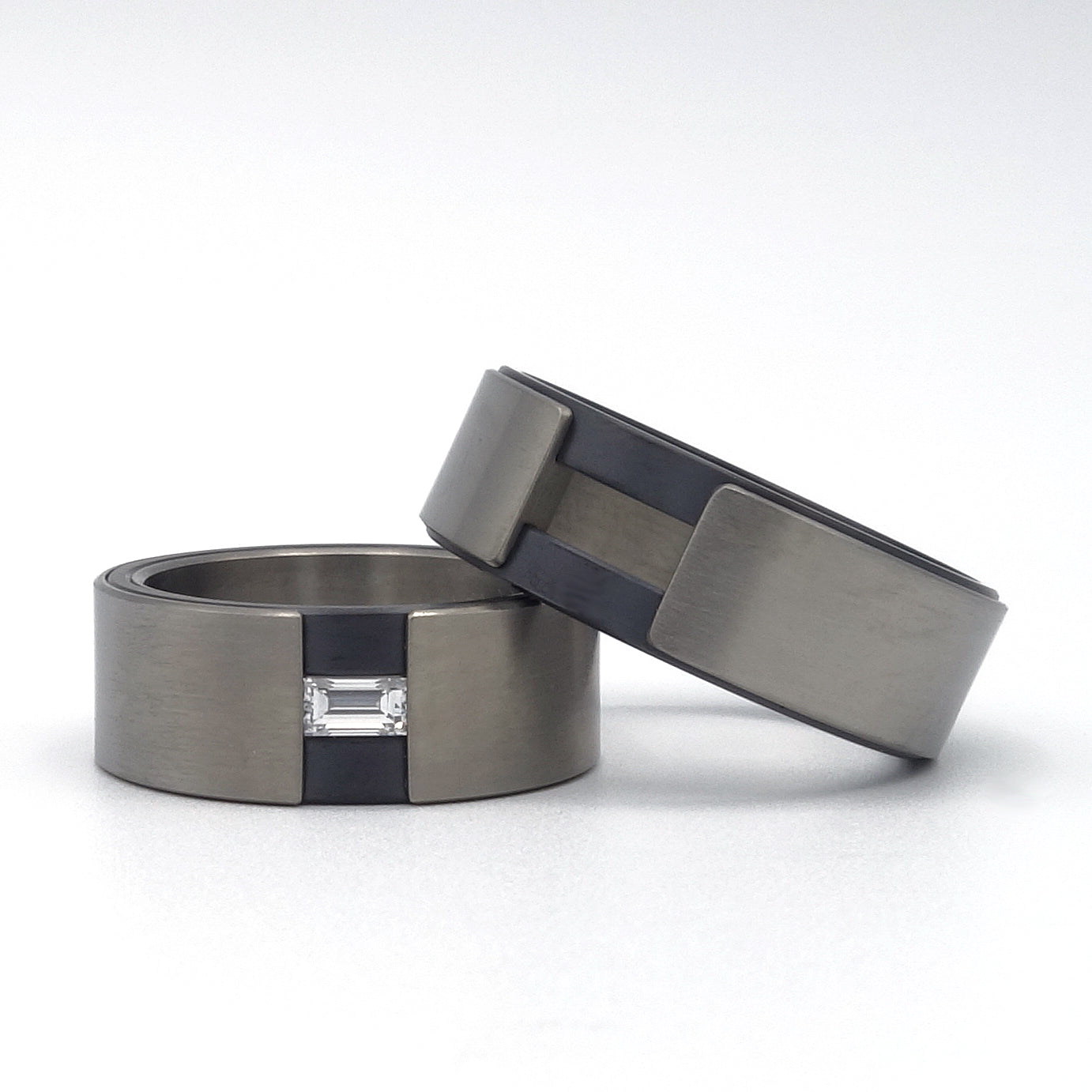 Set van moderne trouwringen in titanium en zirkonium, met baguette-geslepen diamant in de ene ring, strak tegen elkaar geplaatst.