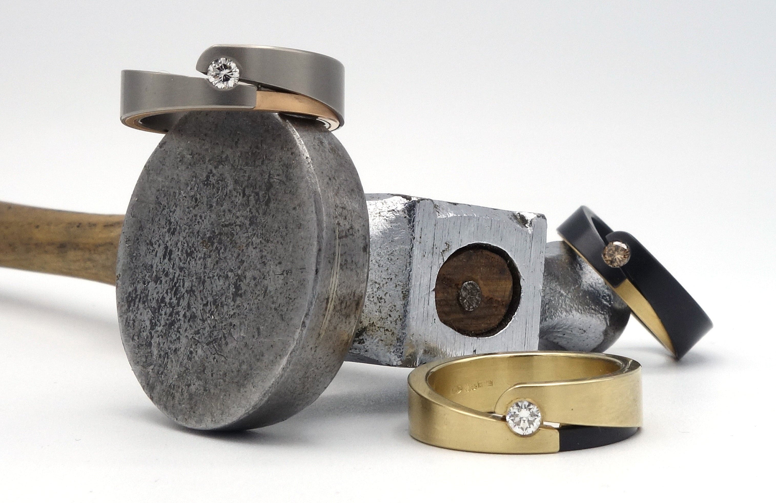 Collectie moderne ringen met diamant op een smeedhamer – symbool voor vakmanschap en maatwerk bij Metal Art Sieraden.