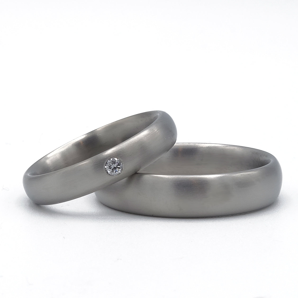 Matte titanium trouwringen in ovale vorm, damesring met 0.05 ct witte diamant en herenring van 6 mm breed.
