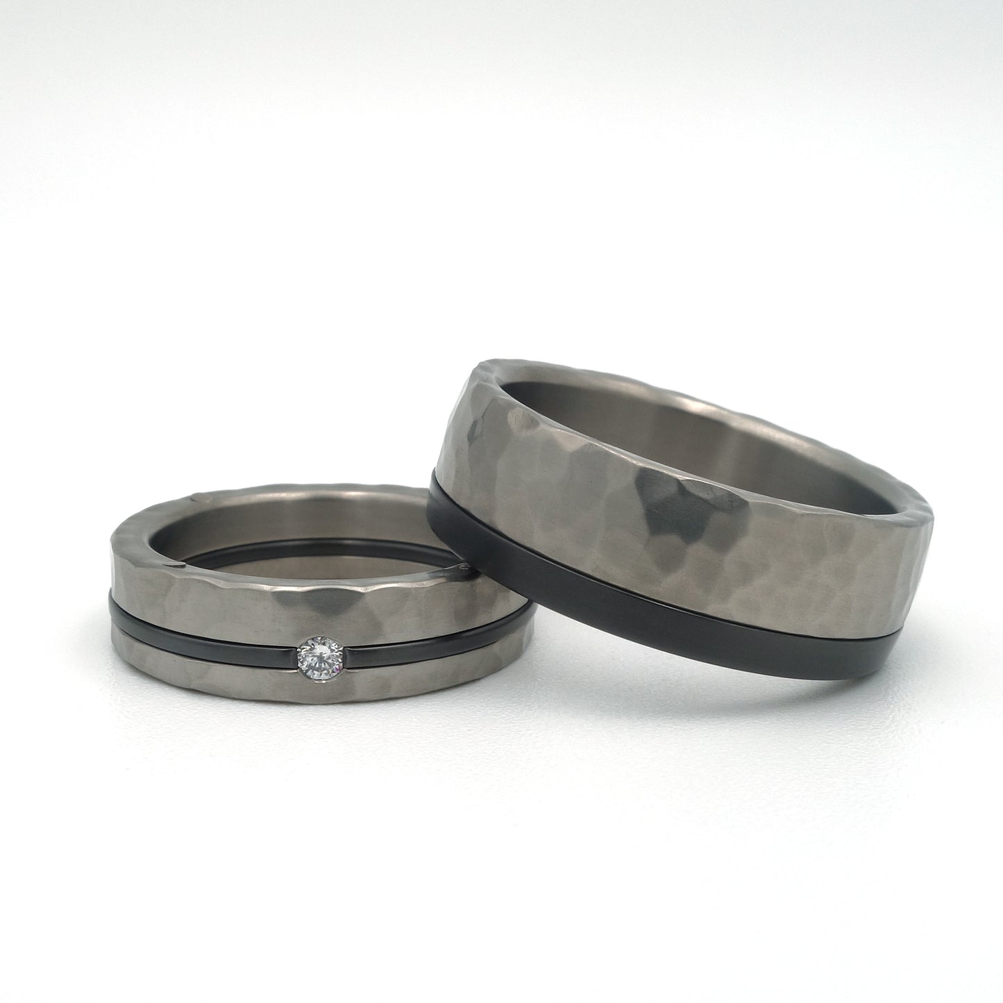 Titanium hamerslag ringen met zwarte lijn; damesring met diamant 0.03 ct en witgouden details, herenring met zwarte lijn aan de zijkant.