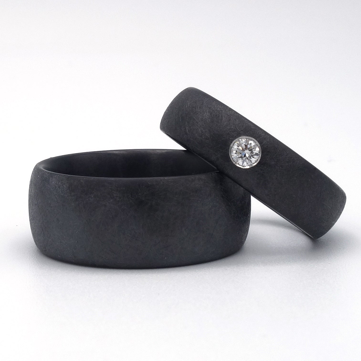 Zwarte zirkoniumringen met matte krasstructuur; één met diamant van 0.08ct in verzonken zetting