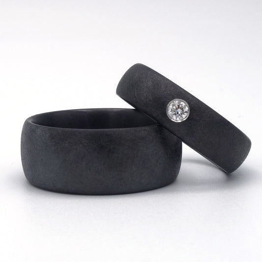Zwarte zirkoniumringen met matte krasstructuur; één met diamant van 0.08ct in verzonken zetting