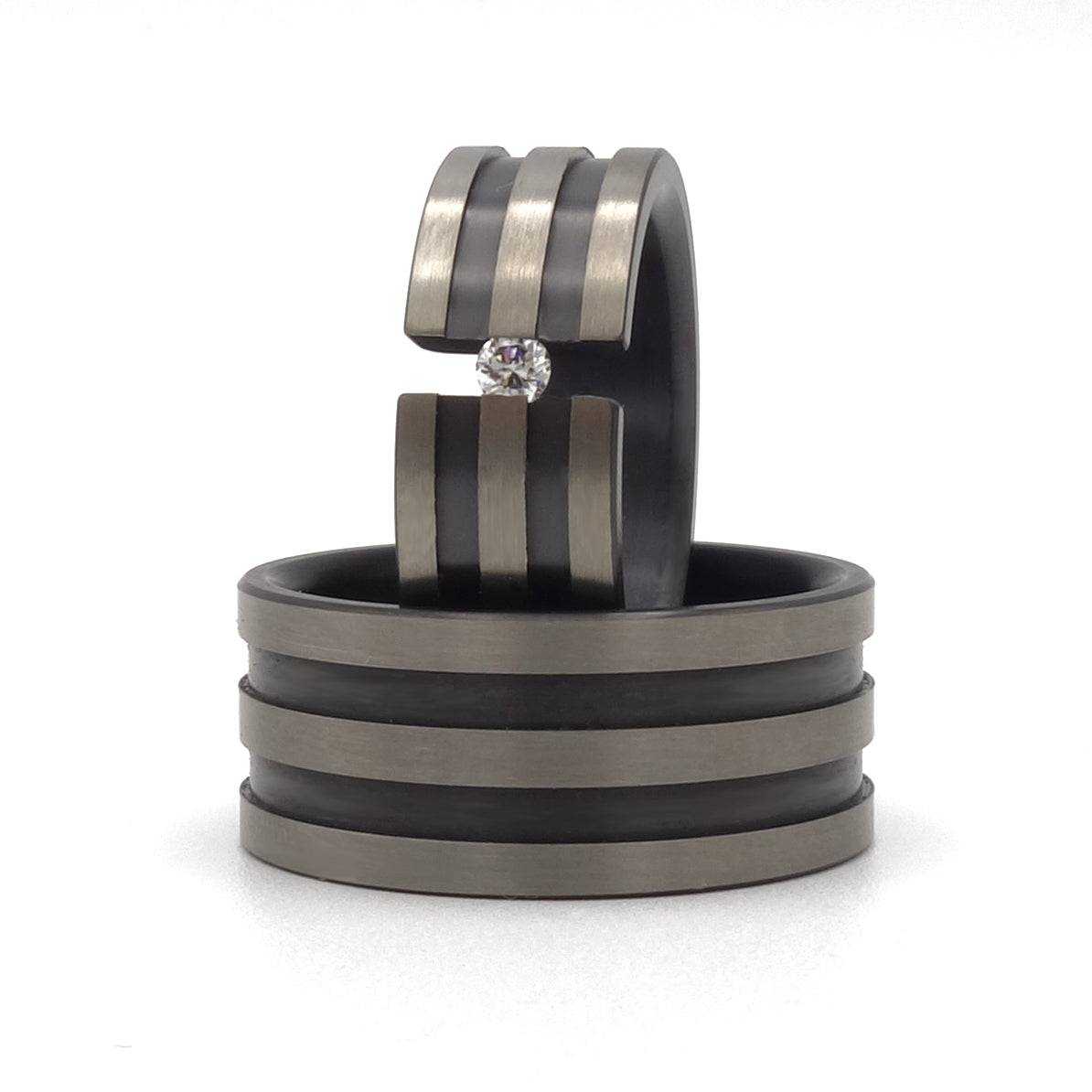 Twee brede zirkoniumringen met drie groeven; één met een briljant van 0.08ct in optische spanzetting met bruggetje