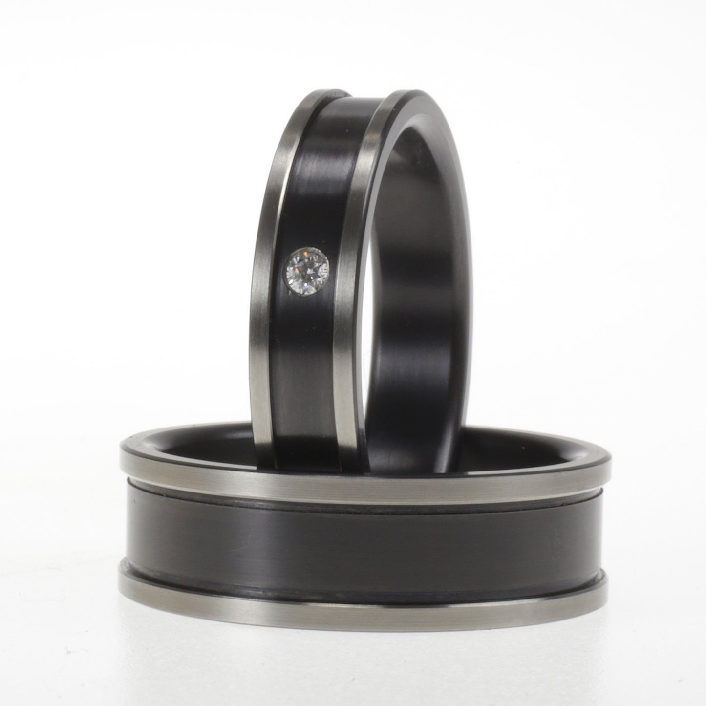 Set zwarte zirkonium trouwringen, één met diamant en één zonder, met glanzende randen en matte kern.