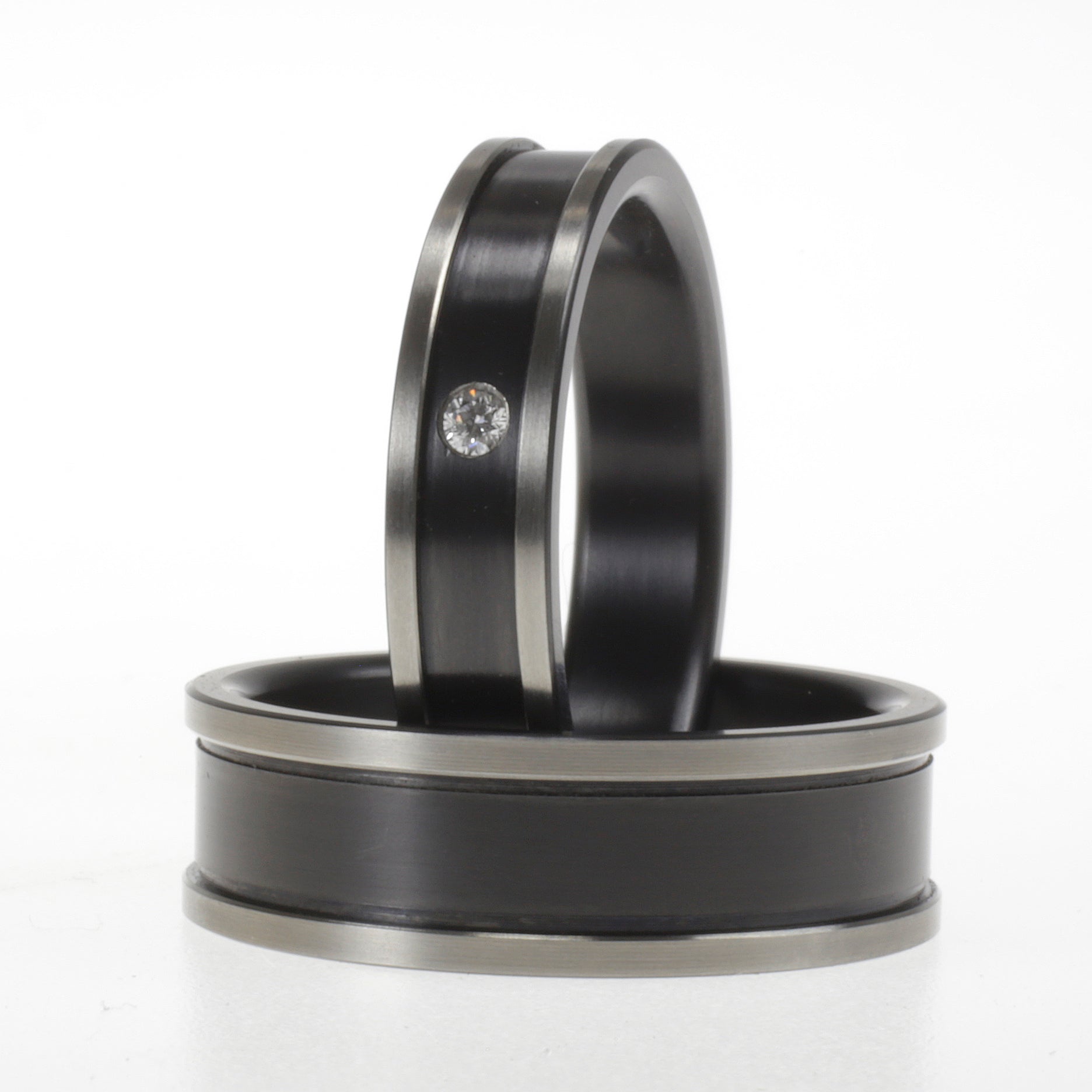 Set zwarte zirkonium trouwringen, één met diamant en één zonder, met glanzende randen en matte kern.