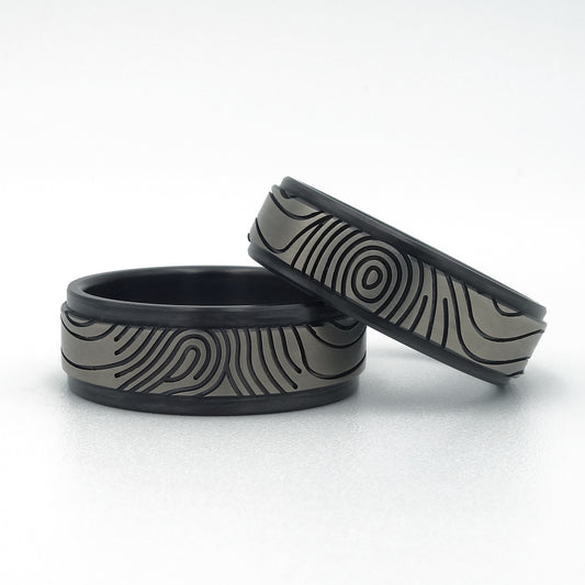 Twee zirkonium vingerafdruk trouwringen in zwart-grijs contrast met rechte vorm en zwarte randen.