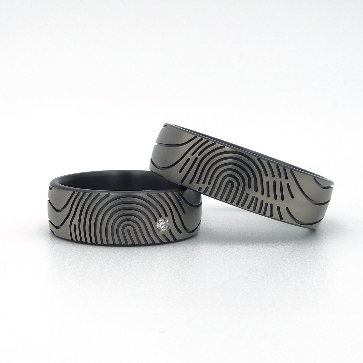 Twee moderne zirkonium trouwringen met vingerafdrukdesign, waarvan één met diamantaccent.