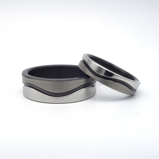 Twee trouwringen uit de Wave-serie van zwart zirkonium en edelstaal met golvend ontwerp, in breedtes van 4 en 7 mm, samen gepresenteerd.