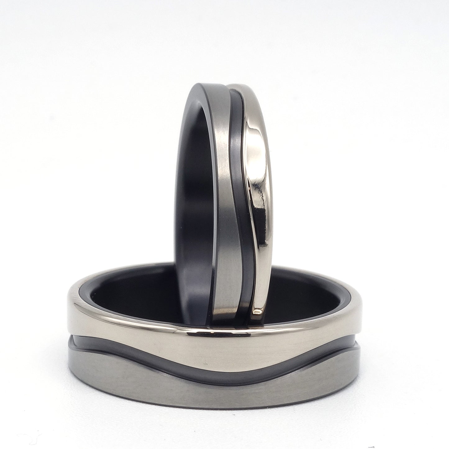 Twee trouwringen met golvend ontwerp van zwart zirkonium en 14 karaat witgoud, in 4,5 mm en 7 mm breedte, samen gepresenteerd.