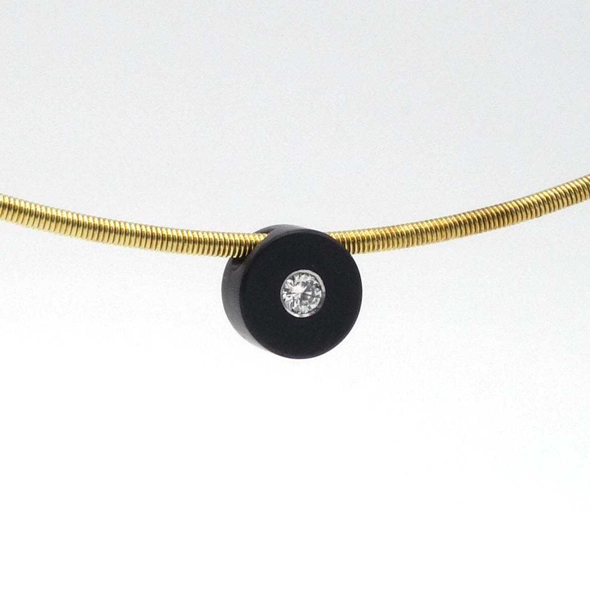 Zwarte zirkonium hanger van 7,5 mm met witte diamant van 0,05 ct, aan een goudkleurige spang.