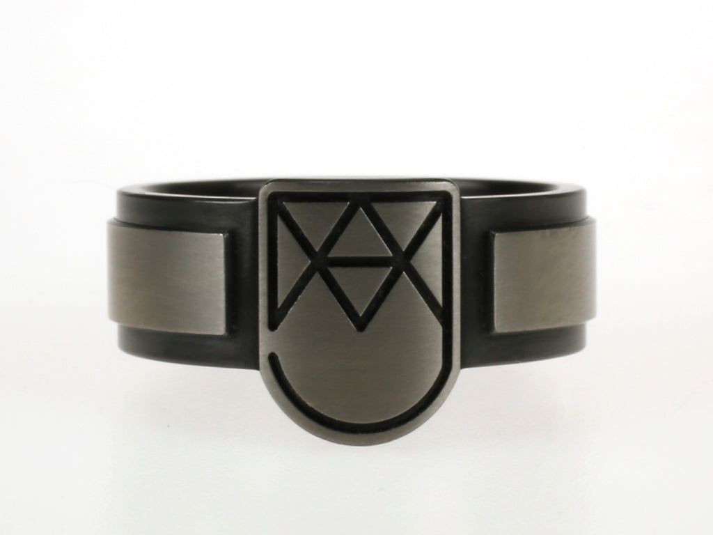 Moderne monogramring met schildvorm en abstracte initialen, uitgevoerd in titanium en zirkonium