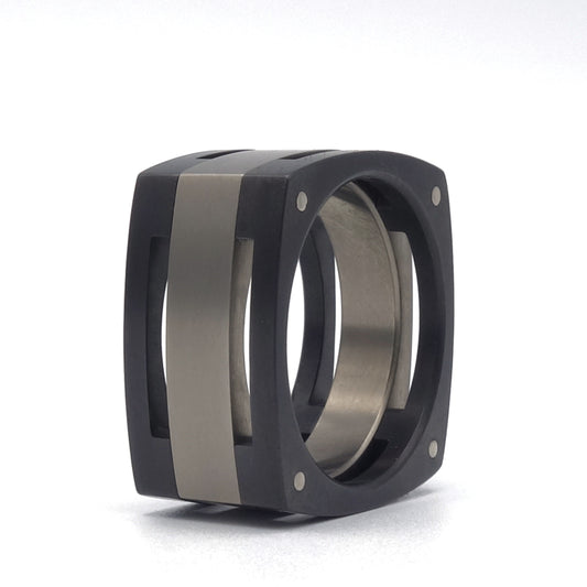 Vierkante Blok-ring Fracine van zwart zirkonium en grijs titanium met witgouden klinknagels en opengewerkte zijvlakken.