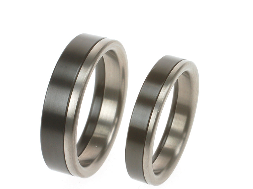 Strakke trouwringen van titanium en zwart zirkonium met verdiepte lijn als detail.