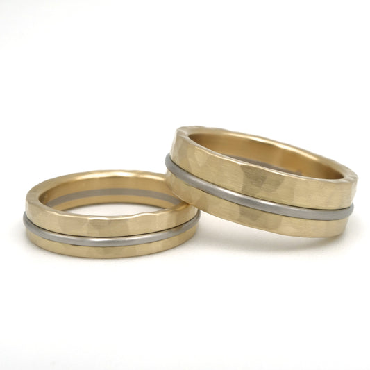 Set trouwringen in 18kr geelgoud met hamerslag structuur en gladde witgouden middenlijn. Twee breedtes, mat geelgoud met gepolijst witgoud als contrast.