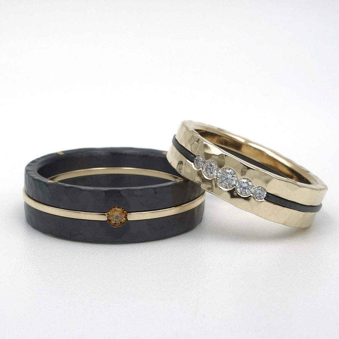  Set trouwringen in zwart zirkonium en 14kr geelgoud met hamerslag structuur. Herenring met cognac diamant in gouden middenlijn, damesring met vijf witte diamanten glad omgezet in geelgoud.