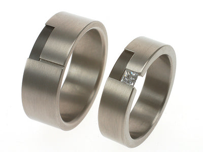 Set moderne titanium ringen met strakke uitsparing; één ring uitgevoerd met een prinses geslepen diamant, de andere in massief titanium zonder steen.