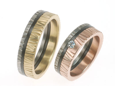 Structuur trouwringen met hamerslag in geelgoud en roodgoud, gecombineerd met een middenbaan van zwart zirkonium; één ring gezet met diamant.