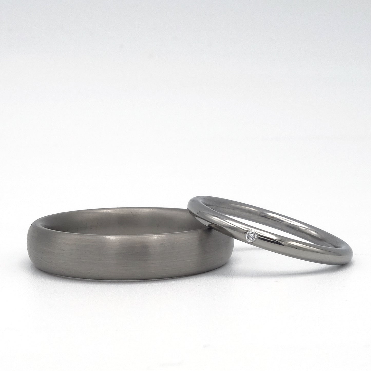 Trouwringenset van titanium, met ovale matte herenring en slanke damesring met glans en diamant van 0.01 ct.