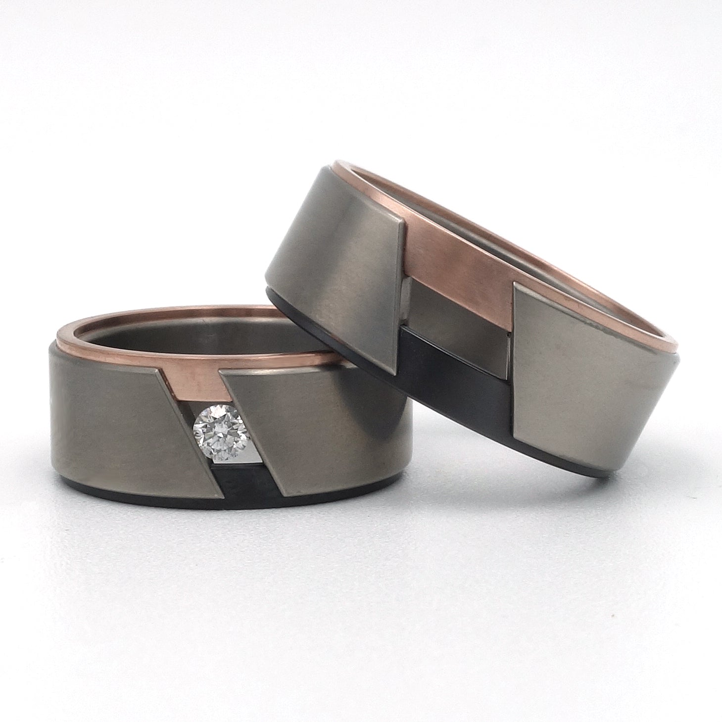 Set trouwringen Zem in titanium met zwart zirkonium en roodgoud zij-insteek; de damesring gezet met een diamant van 0.10ct.