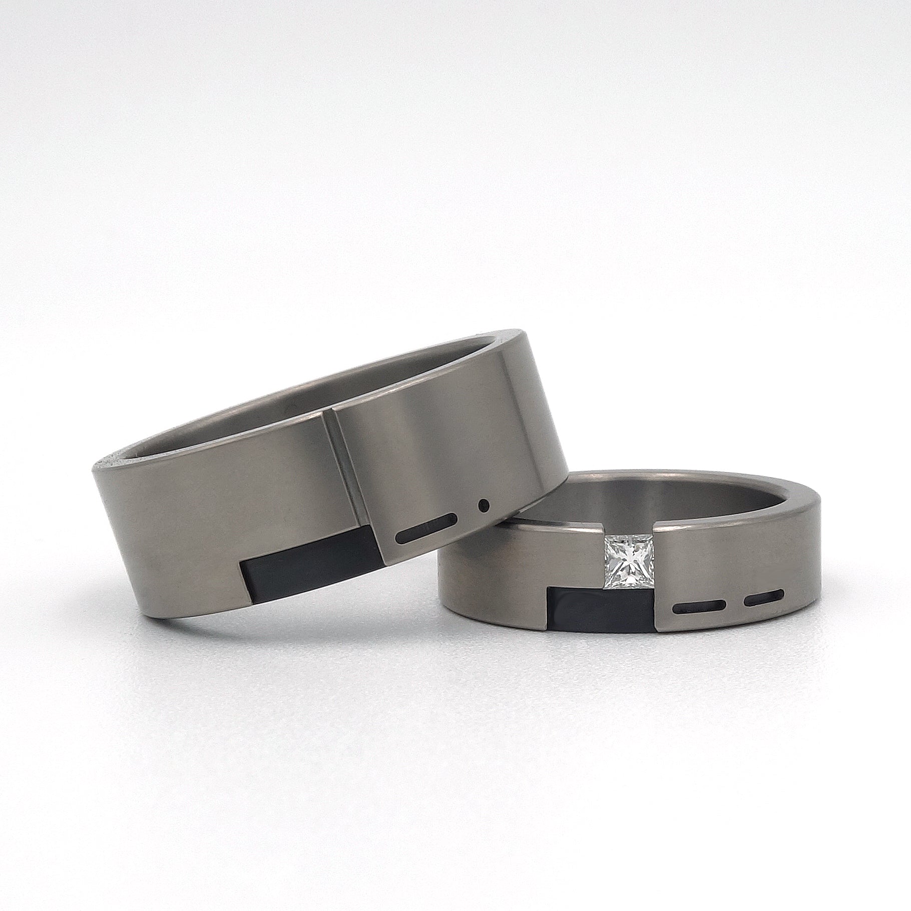 Set trouwringen Leona & Leon in titanium met zwart zirkonium, met de voorletter van de partner verwerkt in morsecode; Leona gezet met een prinsesgeslepen diamant van 0.15ct.