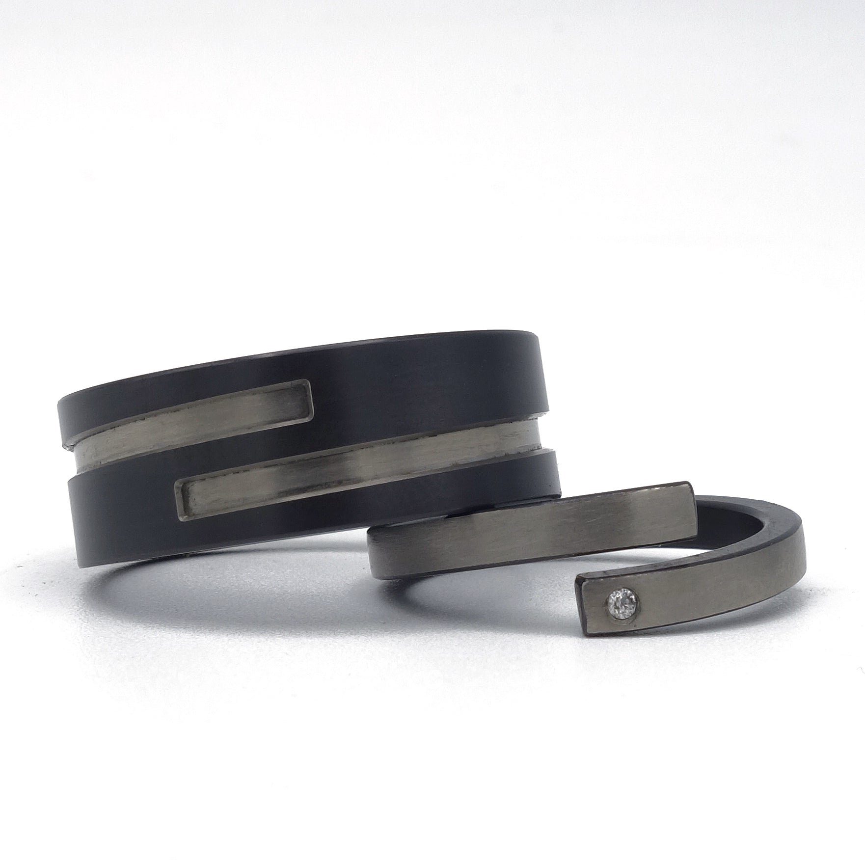 Set moderne trouwringen in zirkonium met omgekeerde kleuren: brede zwarte ring met grijze inleg en smalle grijze ring met zwarte binnenzijde en diamantje.