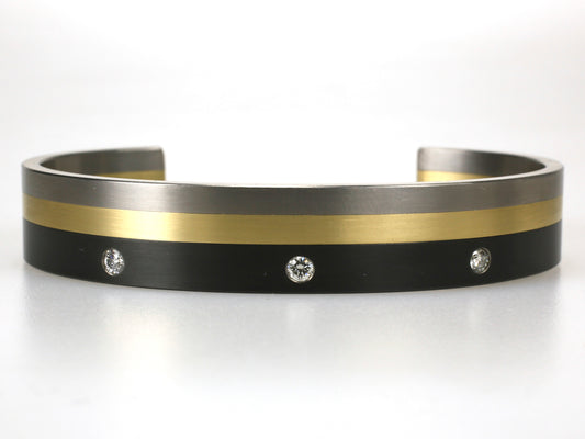 Titanium armband met zwart en geelgoud, voorzien van drie diamanten in zwarte titaniumlaag, strak en modern ontwerp.