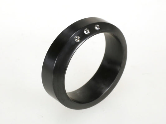 Volledig zwarte zirkonium ring met drie kleine diamanten in een rechte lijn geplaatst.