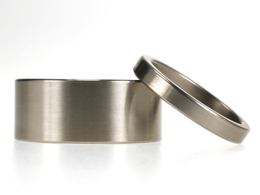 Titanium trouwringenset met brede 9 mm herenring en smalle 3 mm damesring, beide met matte afwerking.