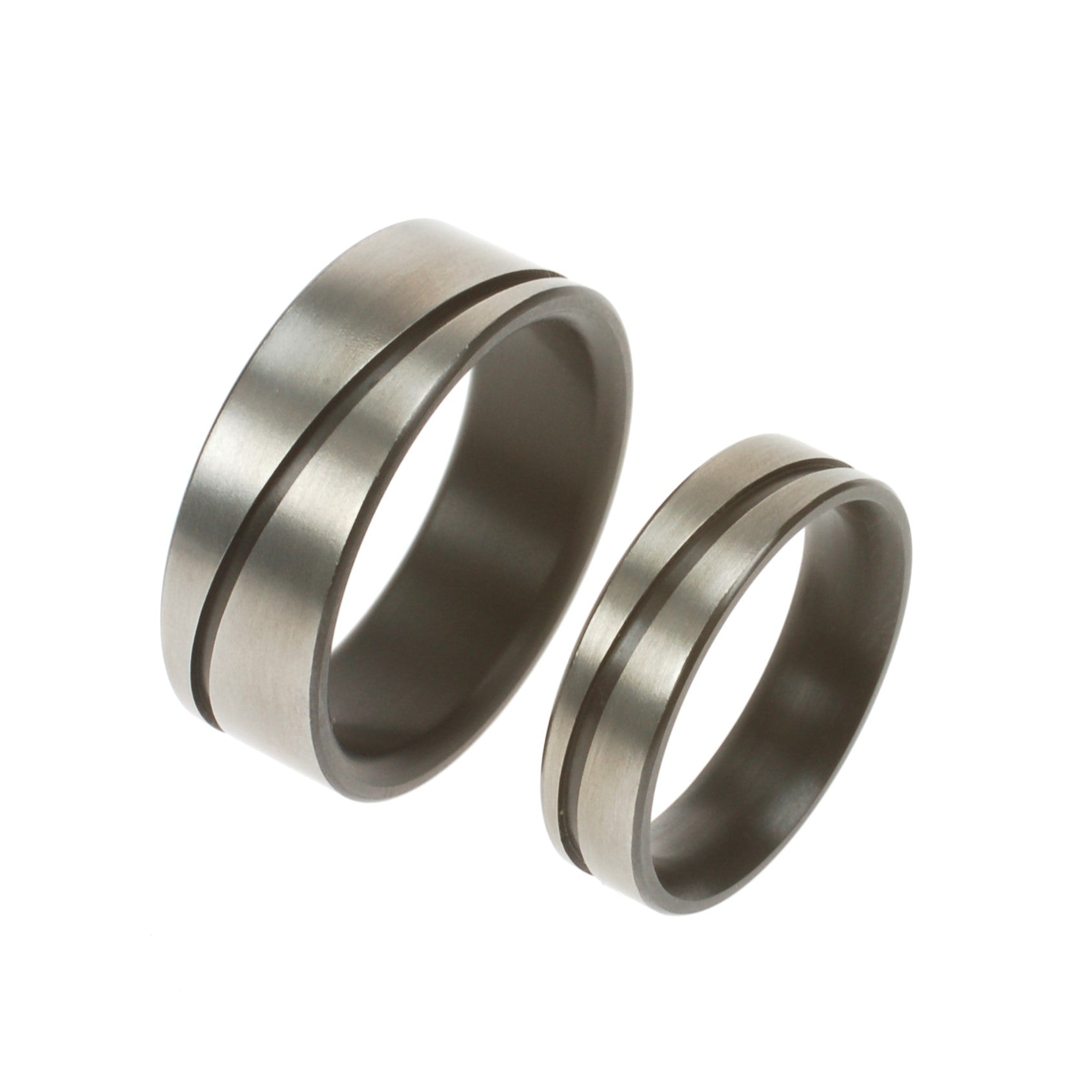 Twee zirkoniumringen met diagonale groef; één van 5 mm en één van 8 mm breed, beide zonder diamant en mat afgewerkt.