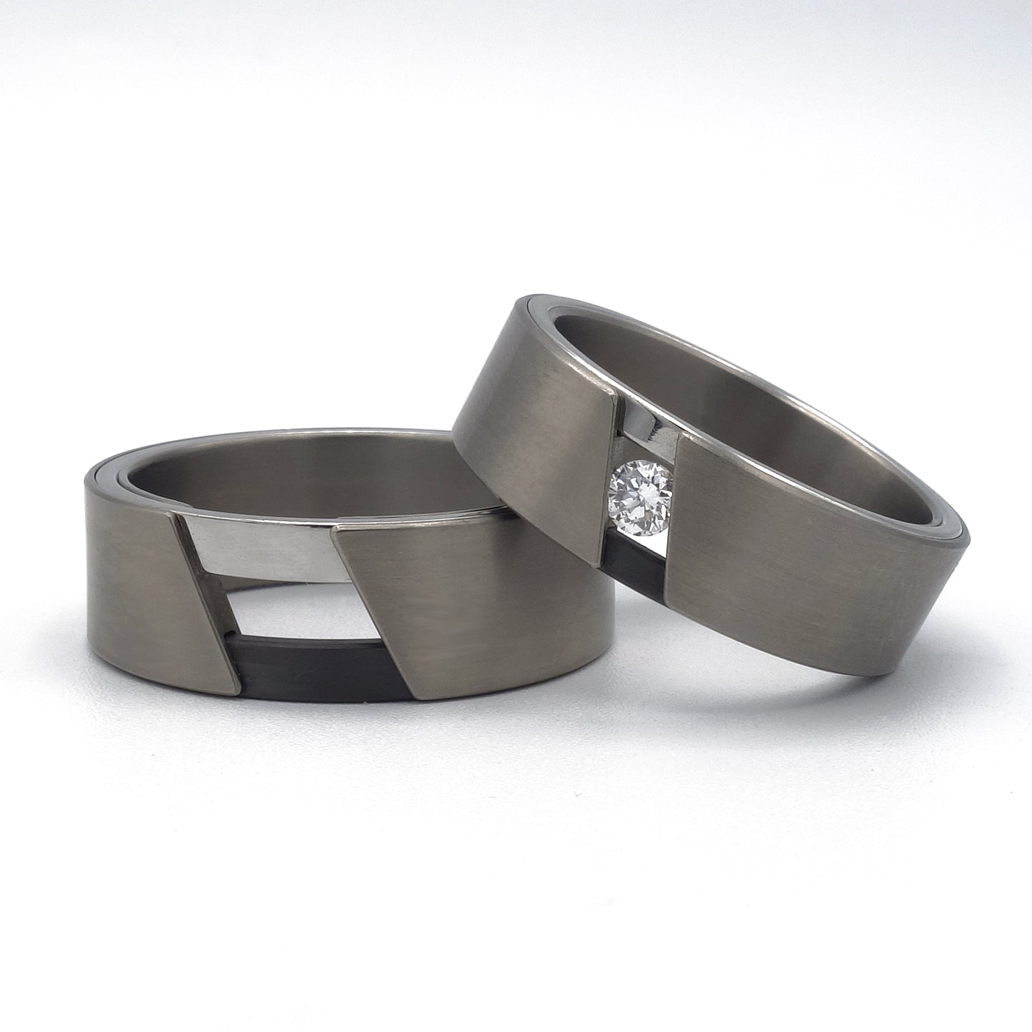 Twee moderne ringen van titanium, zirkonium en glanzend edelstaal; één met diamant van 0.10 ct in driehoekige uitsparing, één zonder.