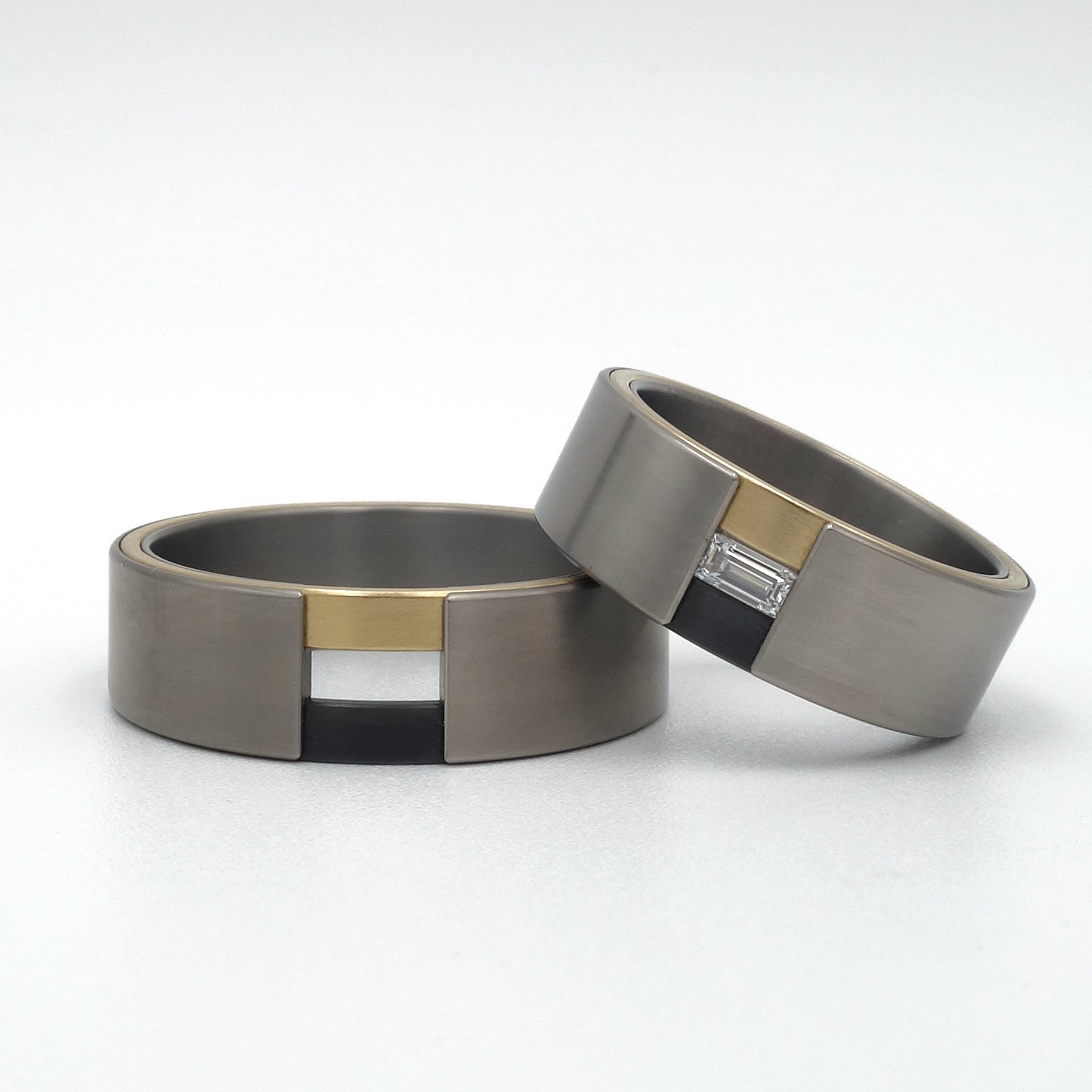 Set trouwringen Edo in titanium met zwart zirkonium en geelgoud zij-insteek, een van de ringen gezet met een baguette diamant.