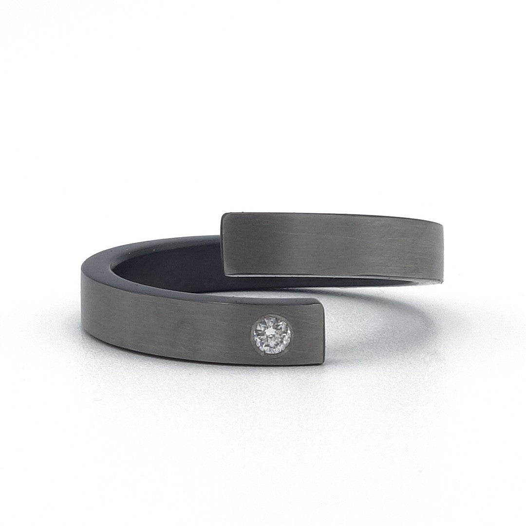 Open zirkonium ring met grijze bovenkant, zwarte zijkanten en een kleine diamant van 0,02 ct – modern, technisch en elegant.
