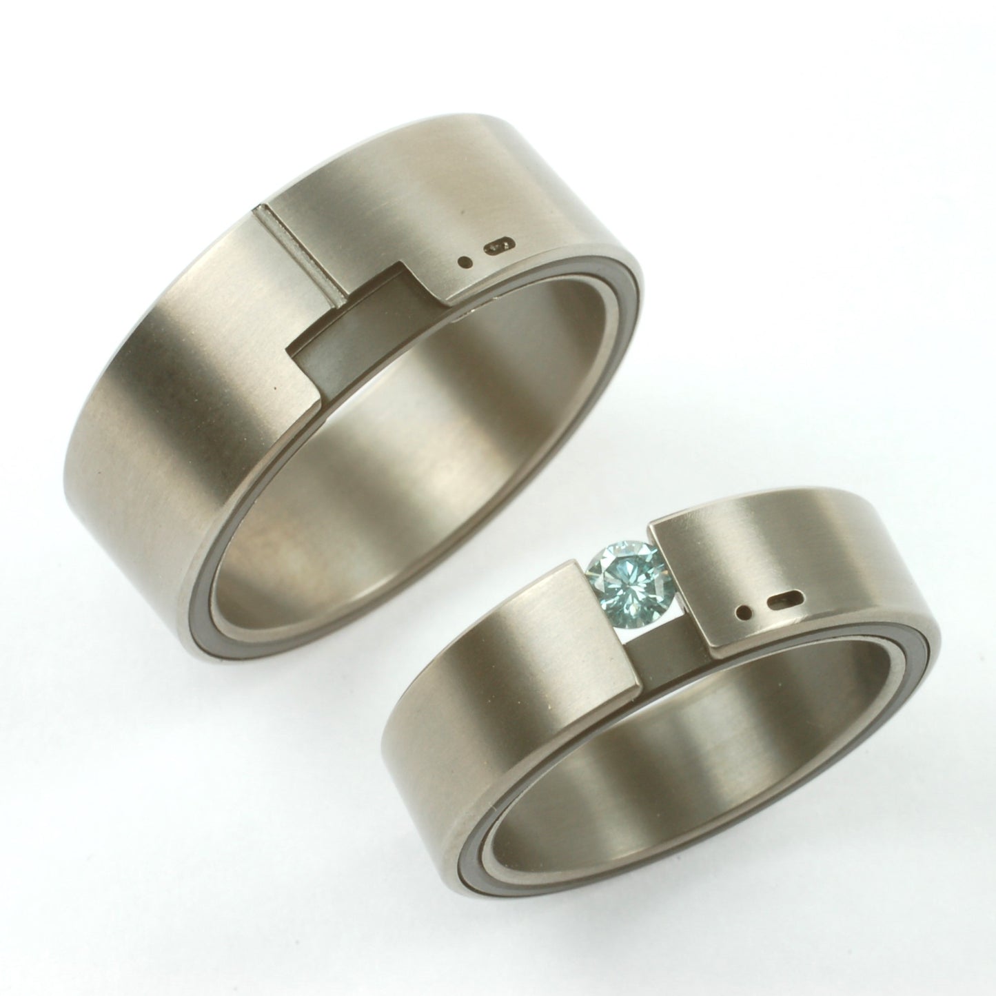 Moderne trouwringen van titanium en zirkonium met Morse-code detail en blauwe briljant in de ene ring.