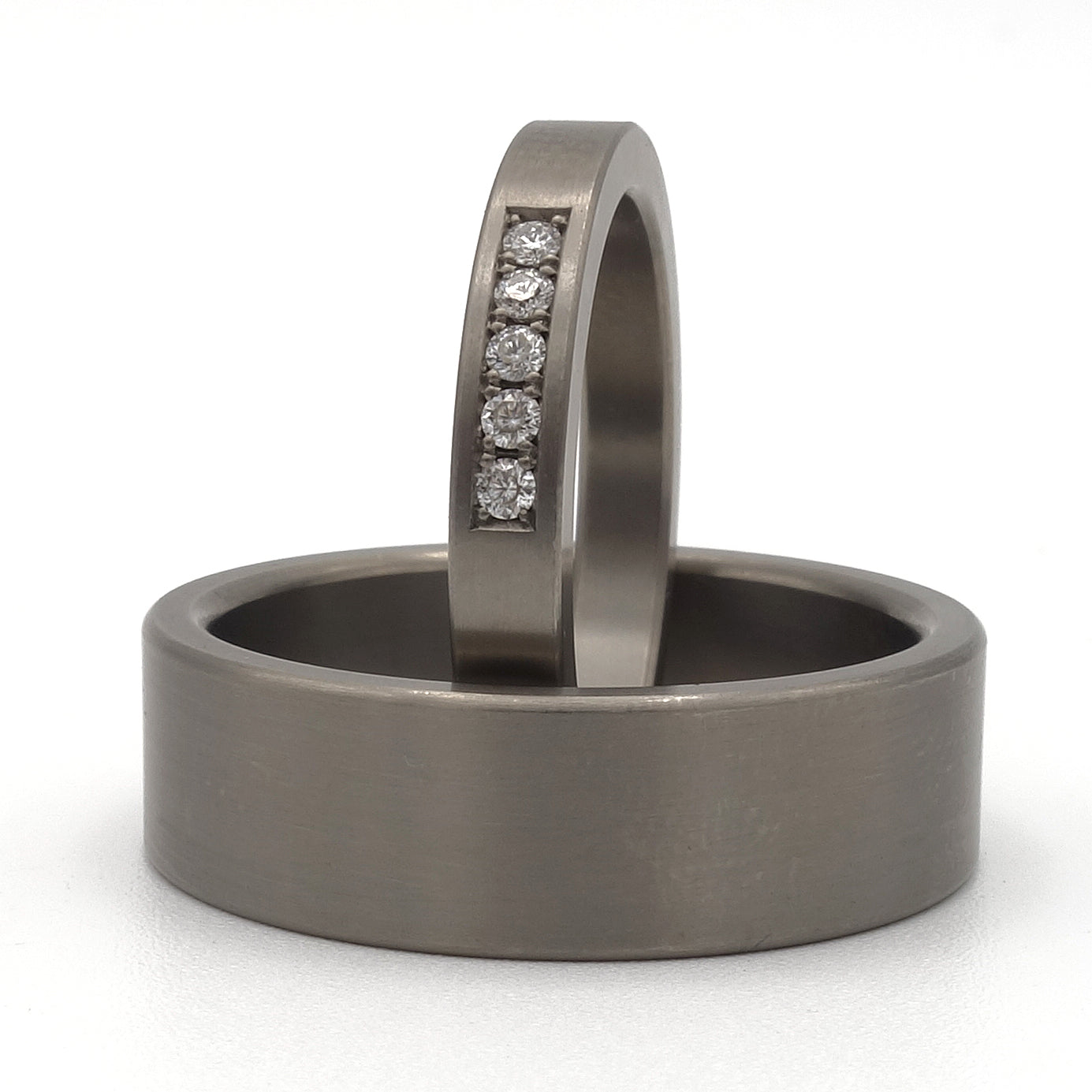 Trouwringenset van titanium met damesring met vijf pavé gezette diamanten en brede 7 mm herenring zonder stenen.