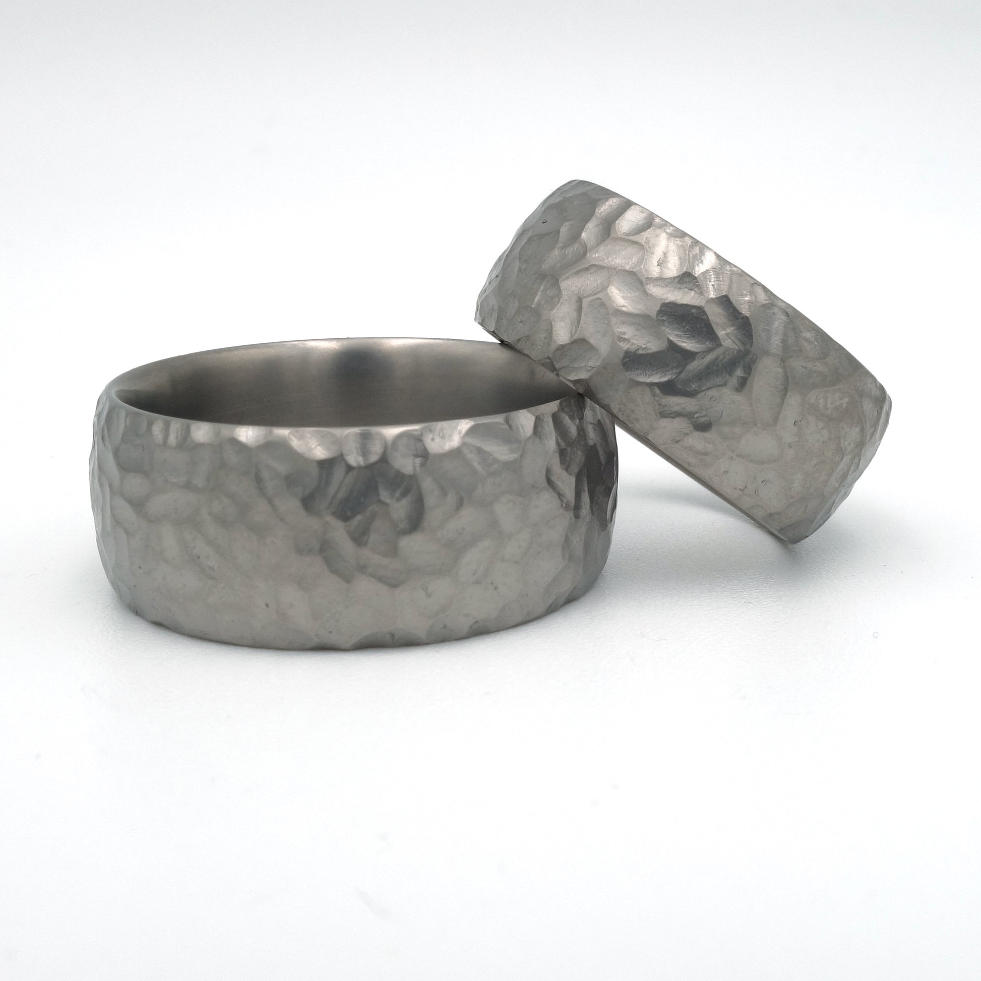 Brede titanium trouwringen met grof hamerslagpatroon; damesring 8 mm, herenring 10 mm.