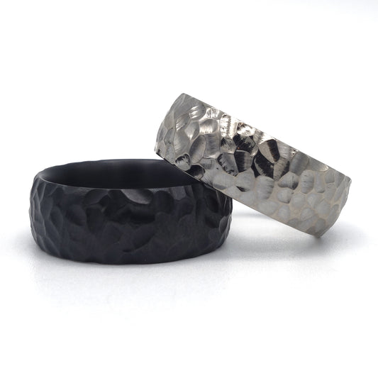 Twee ringen met grove hamerslag: glanzend palladium en mat zwart zirkonium, beide 8 mm breed.