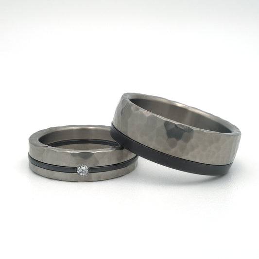 Titanium hamerslag ringen met zwarte lijn; damesring met diamant 0.03 ct en witgouden details, herenring met zwarte lijn aan de zijkant.