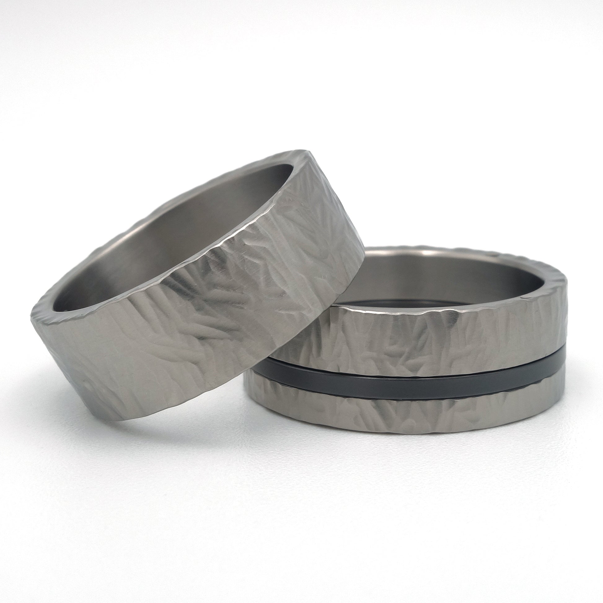 Set van twee titanium ringen met hamerslagstructuur, één met zwarte zirkonium lijn en witgouden klinknagels, als paar gefotografeerd