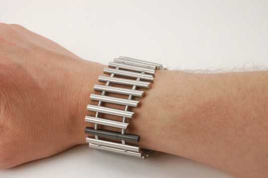 Titanium armband met verticale staven en één zwart zirkonium element, modern technisch ontwerp uit het atelier van Metal Art

Om pols