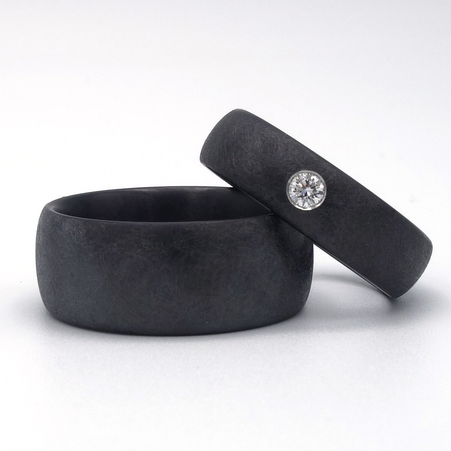 Zwarte zirkoniumringen met matte krasstructuur; één met diamant van 0.08ct in verzonken zetting